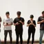 Six young people standing in a row against a wall, every one of them looking at a phone