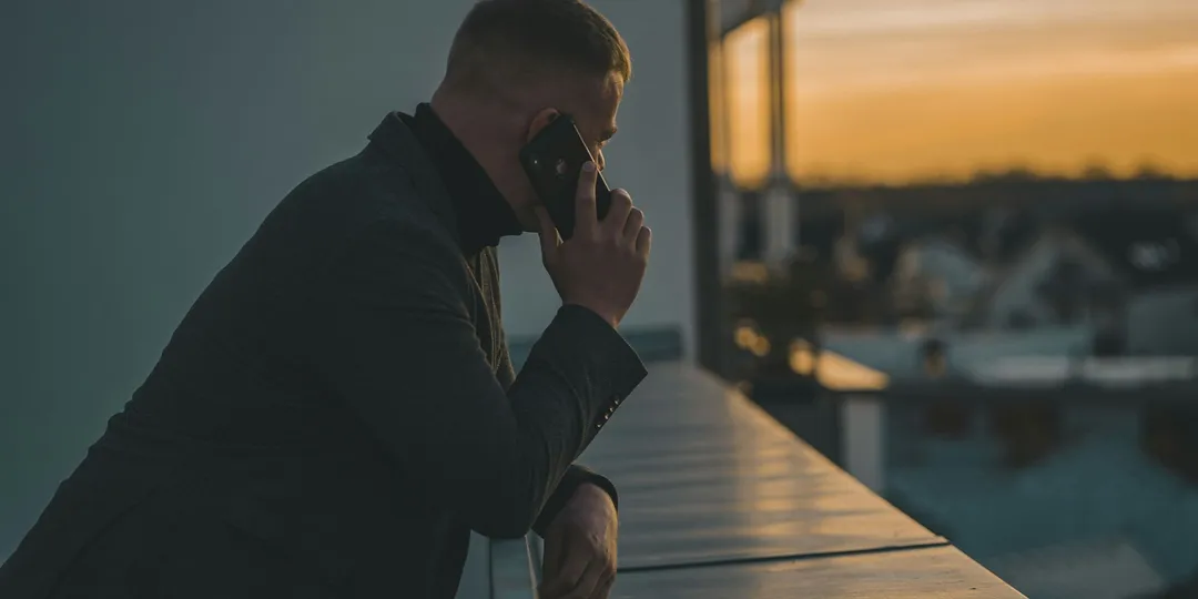 A person on the phone at dusk, leaning on a railing above a city
