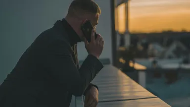 A person on the phone at dusk, leaning on a railing above a city