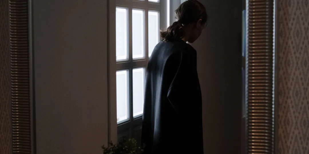 A person seen as a dark reflection in a wall mirror beside a window