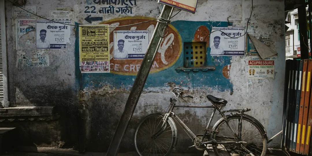 A weathered Indian street wall layered with printed posters, a bicycle propped against it