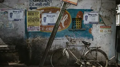 A weathered Indian street wall layered with printed posters, a bicycle propped against it