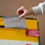 A hand dropping a folded ballot paper into a sealed ballot box
