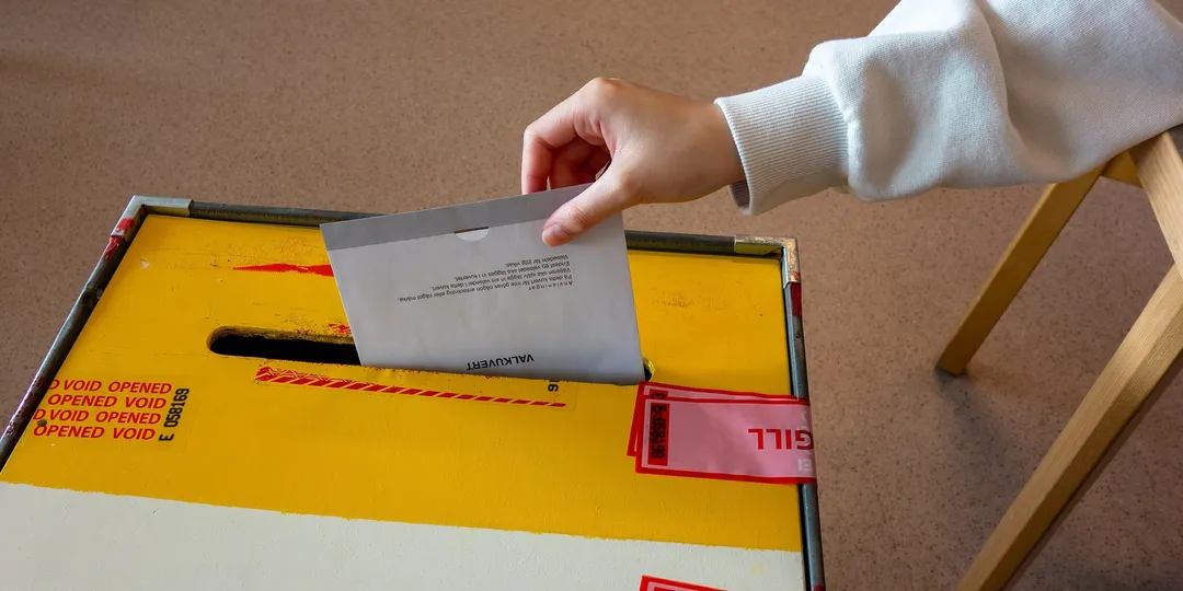 A hand dropping a folded ballot paper into a sealed ballot box