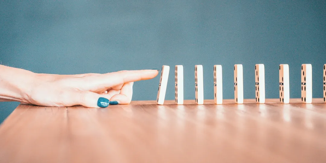 A finger poised to push the first domino in a standing row