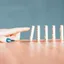 A finger poised to push the first domino in a standing row