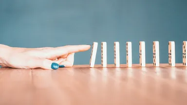 A finger poised to push the first domino in a standing row