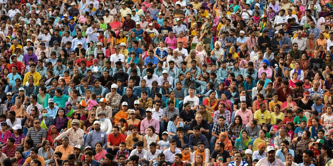 A densely packed crowd of thousands seated at an outdoor gathering in India