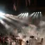 An empty stage set with microphones and music stands, spotlights cutting through haze