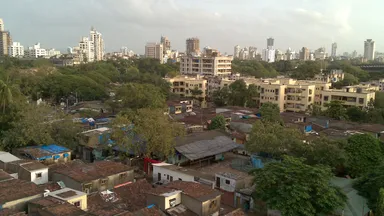Dense low-rise housing in Dharavi, Mumbai, with high-rise blocks on the skyline behind
