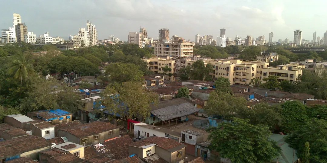 Dense low-rise housing in Dharavi, Mumbai, with high-rise blocks on the skyline behind