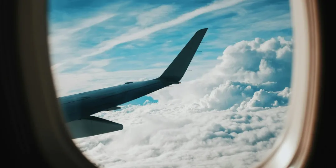 An aircraft wing above a patchwork of green fields, roads and small settlements