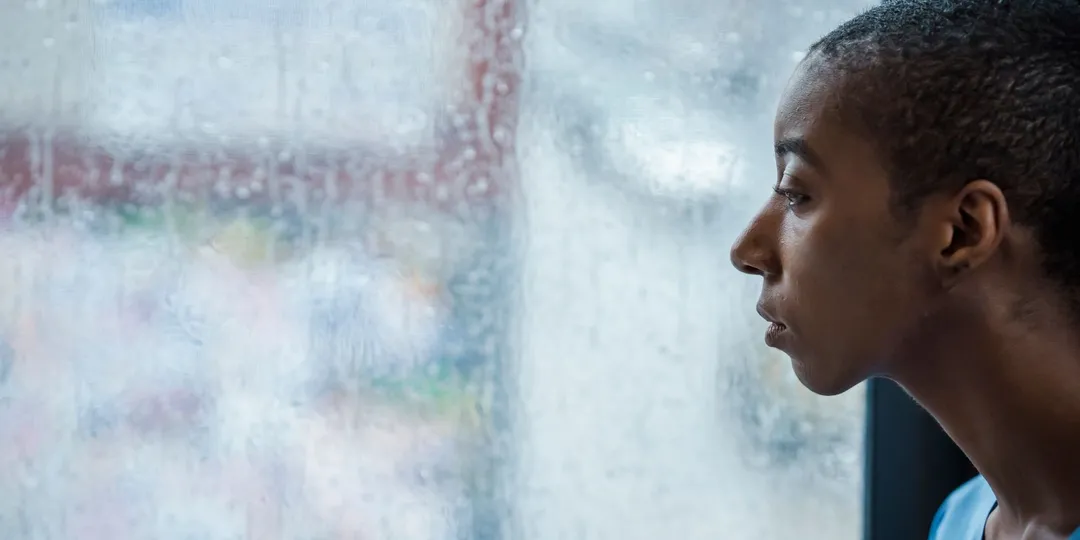A person in profile looking out through a rain-streaked window