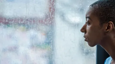 A person in profile looking out through a rain-streaked window