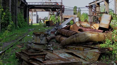 A derelict factory yard with rusted machinery and overgrown ground