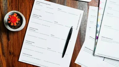A wooden table with loose papers and a pen