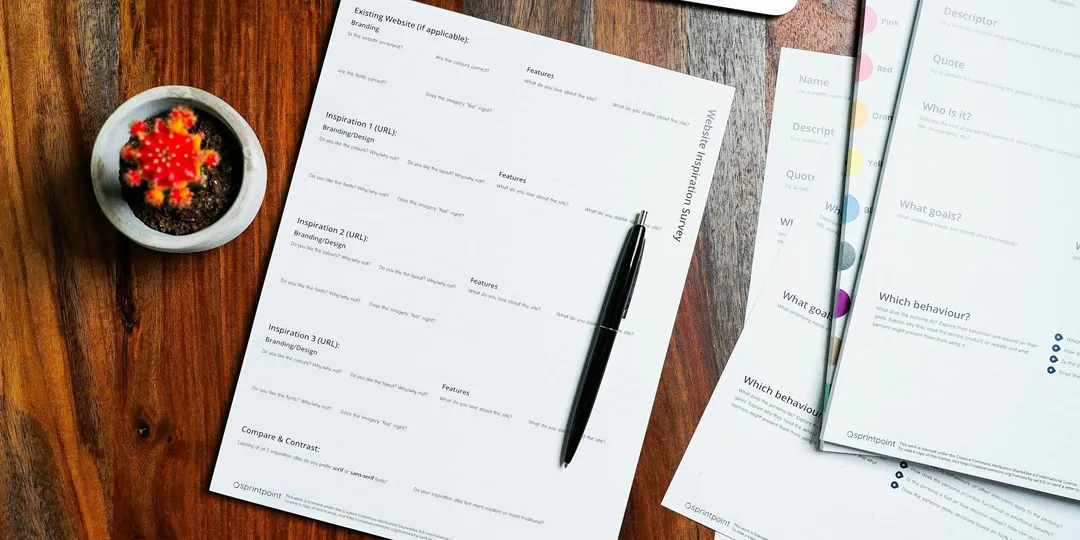 A wooden table with loose papers and a pen