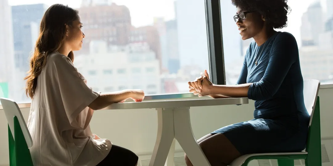 Two people sitting across a table in conversation beside a window