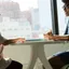 Two people sitting across a table in conversation beside a window