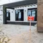 A red 'Home For Sale' sign staked in the gravel yard of a newly built house