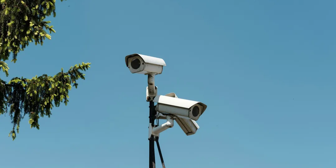 Two surveillance cameras mounted on a pole against a clear sky