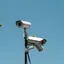 Two surveillance cameras mounted on a pole against a clear sky