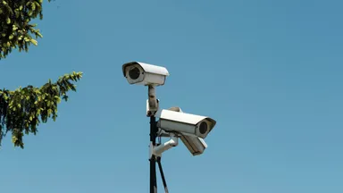 Two surveillance cameras mounted on a pole against a clear sky