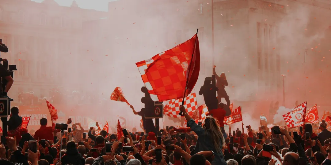 A dense crowd waving flags amid red smoke from flares