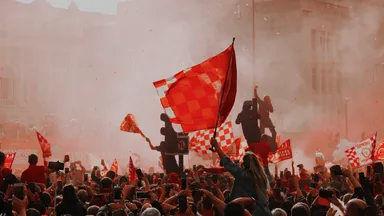 A dense crowd waving flags amid red smoke from flares