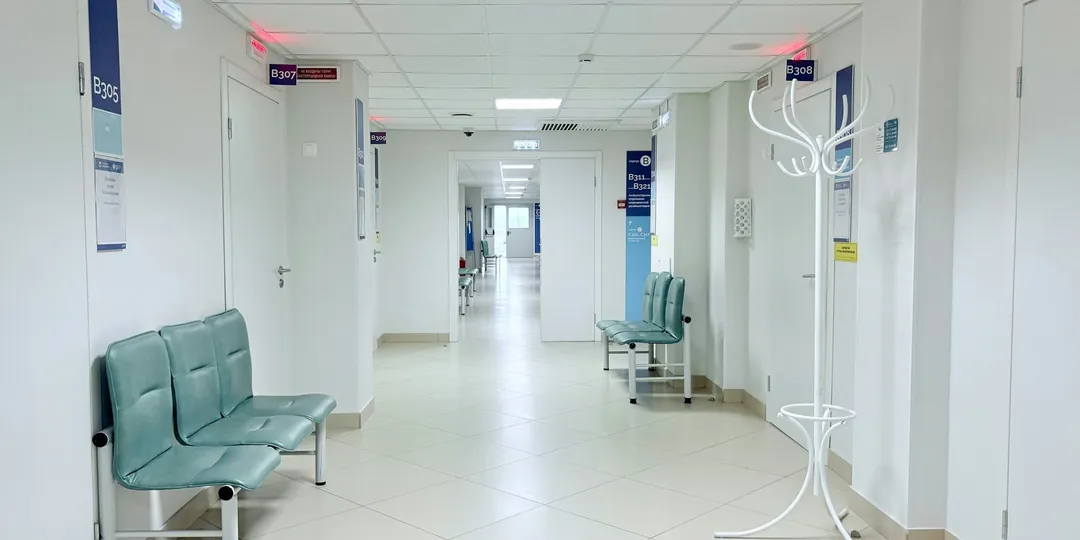An empty hospital corridor lined with benches and closed doors
