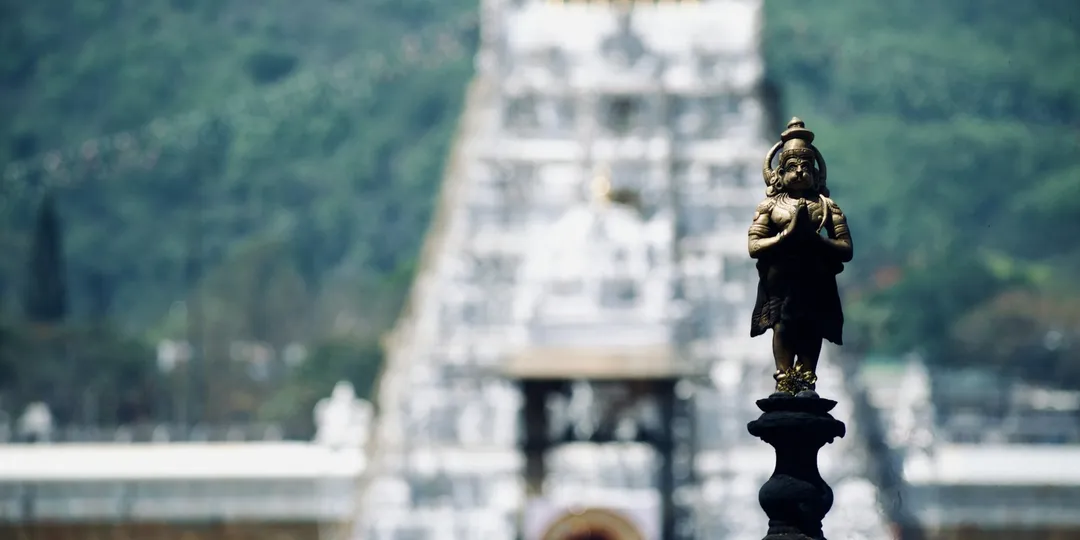 A small gilded deity figure in focus with a temple gopuram blurred behind