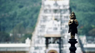 A small gilded deity figure in focus with a temple gopuram blurred behind