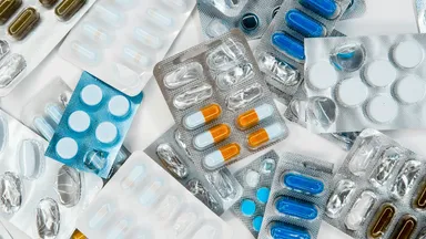 Blister packs of assorted pills and capsules scattered across a surface