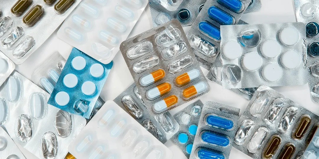 Blister packs of assorted pills and capsules scattered across a surface