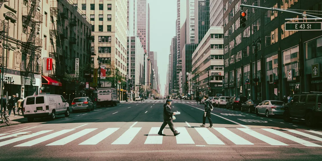 A pedestrian crossing a wide city street at a marked crosswalk, with traffic signals overhead