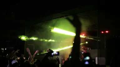 Silhouetted concertgoers raise their hands toward a brightly lit stage.