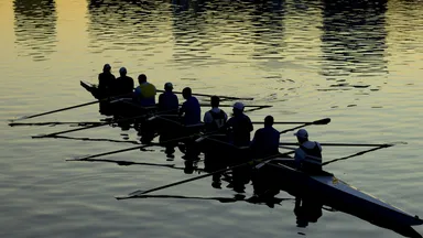 A rowing eight in silhouette on dark water, oars mid-stroke