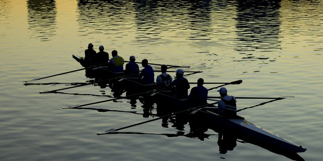 A rowing eight in silhouette on dark water, oars mid-stroke