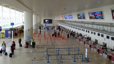 An airport departure concourse with empty queue barriers leading to check-in desks