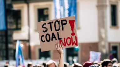 A protester holds a large Stop Coal Now sign above a gathered crowd