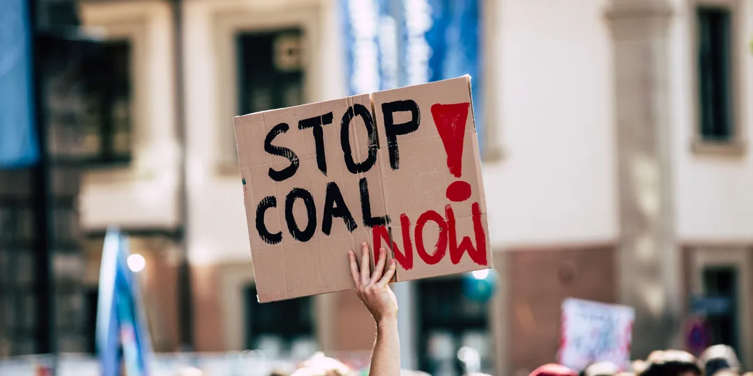 A protester holds a large Stop Coal Now sign above a gathered crowd