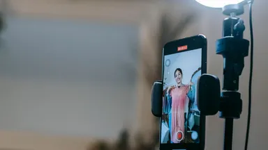 A smartphone mounted on a tripod, the person it is filming visible only on its screen