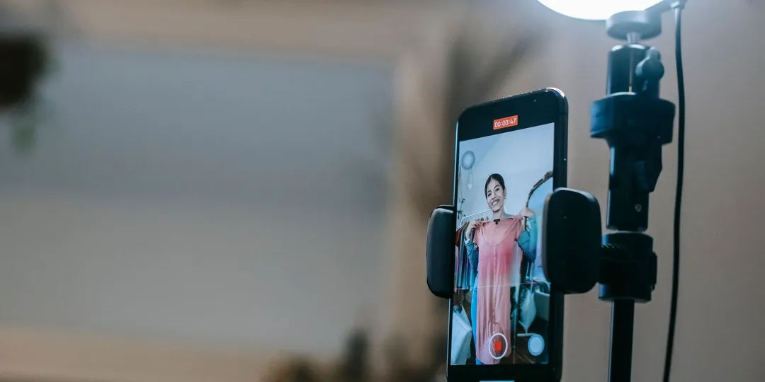 A smartphone mounted on a tripod, the person it is filming visible only on its screen