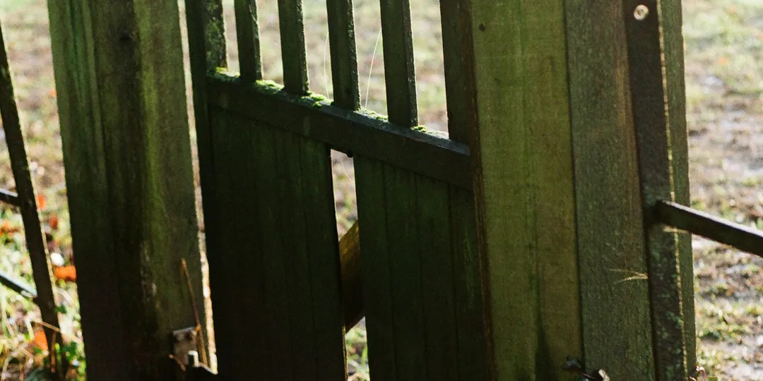 An old wooden gate set into a weathered metal fence in the countryside