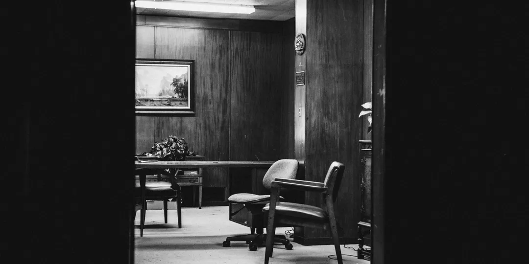 An empty consulting room with chairs and a desk, in black and white