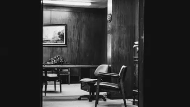 An empty consulting room with chairs and a desk, in black and white