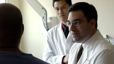 A physician consulting with a patient while another physician takes notes