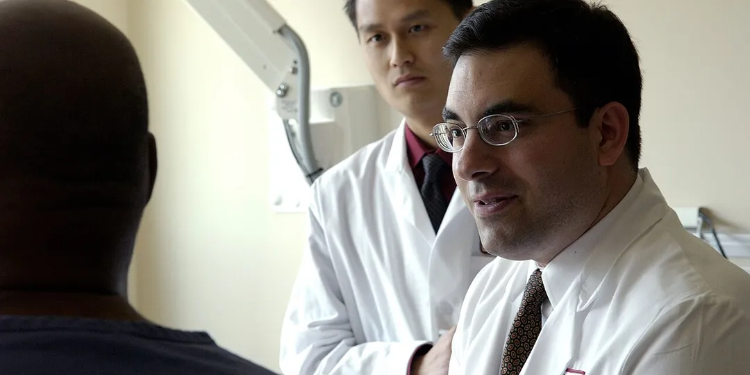 A physician consulting with a patient while another physician takes notes
