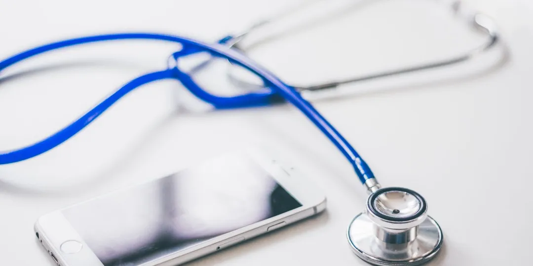 A stethoscope and a smartphone lying side by side on a white surface