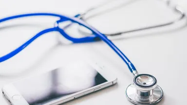 A stethoscope and a smartphone lying side by side on a white surface